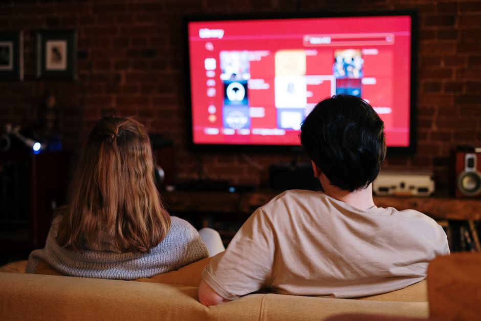 Una pareja disfruta de ver programas en streaming en una gran TV en una acogedora sala de estar con paredes de ladrillo.