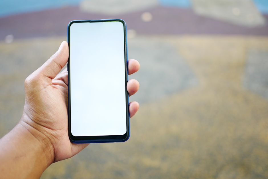 Un primer plano de una mano sosteniendo un smartphone con una pantalla blanca en blanco, al aire libre.