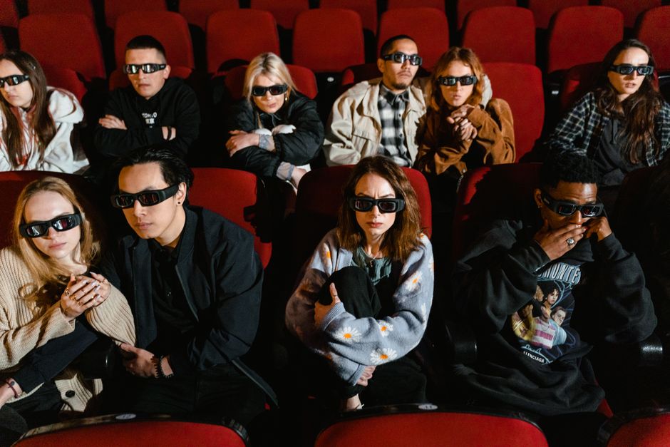 Un grupo diverso de personas usando gafas 3D, inmerso en una película dentro de un cine.