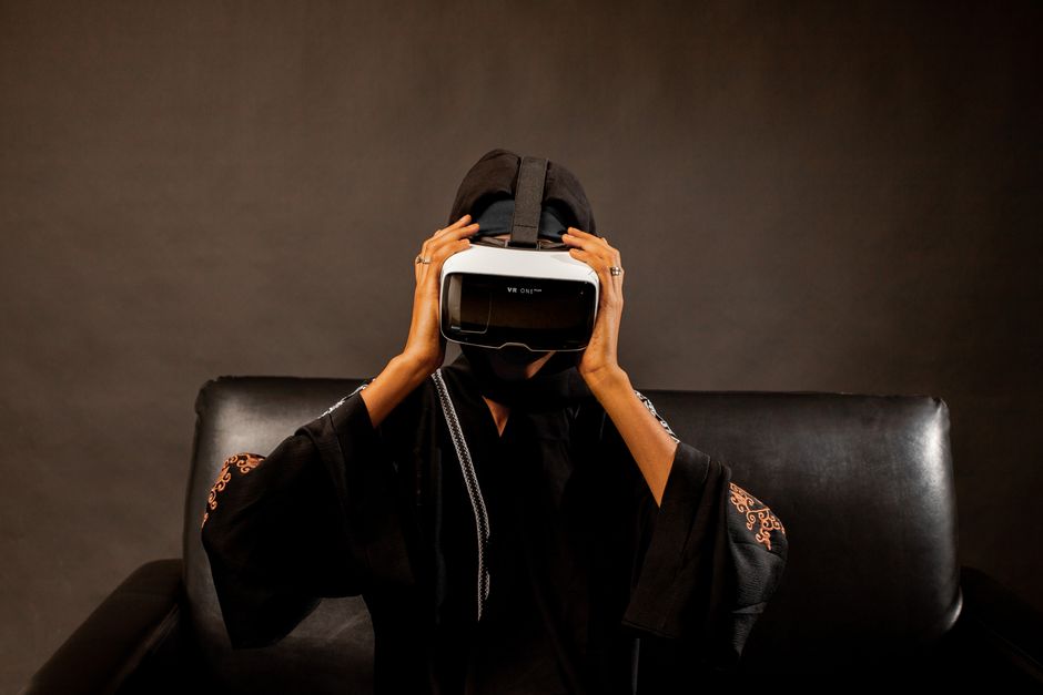 Mujer de Oriente Medio con atuendo tradicional negro explora la realidad virtual con auricular VR.