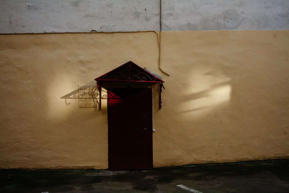 Una puerta roja oxidada delante de una pared amarilla desgastada, iluminada por la luz del sol.