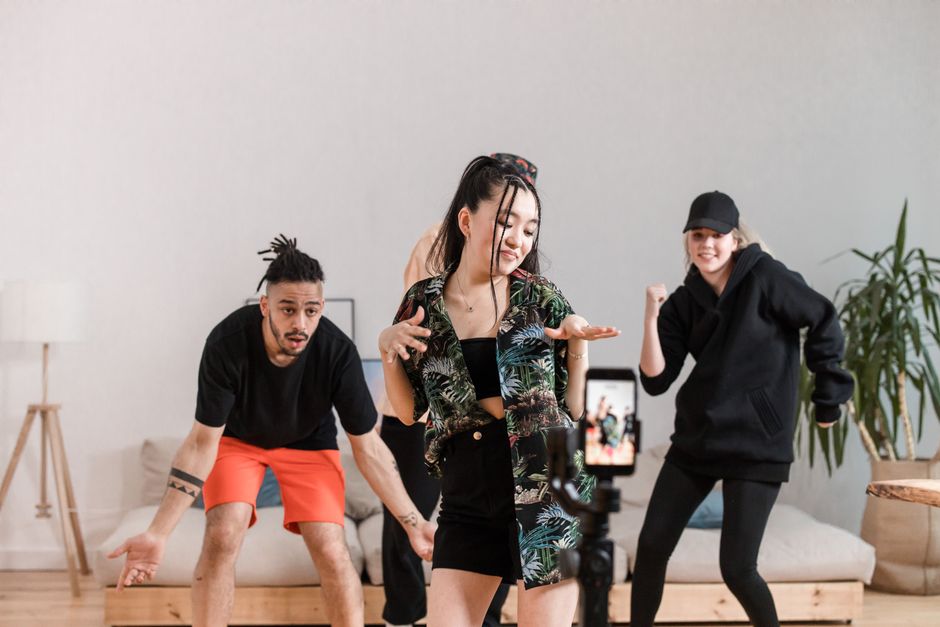 Grupo de jóvenes diversos bailando y grabando contenido en interiores con un smartphone.