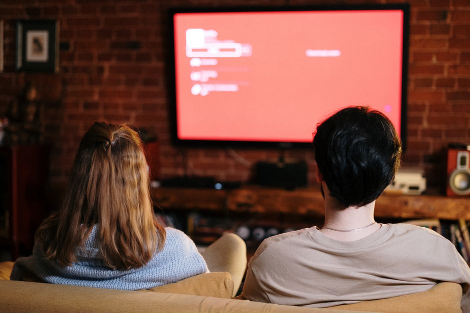 Una pareja ve la televisión junta en una acogedora sala de estar con paredes de ladrillo, sentados en el sofá.