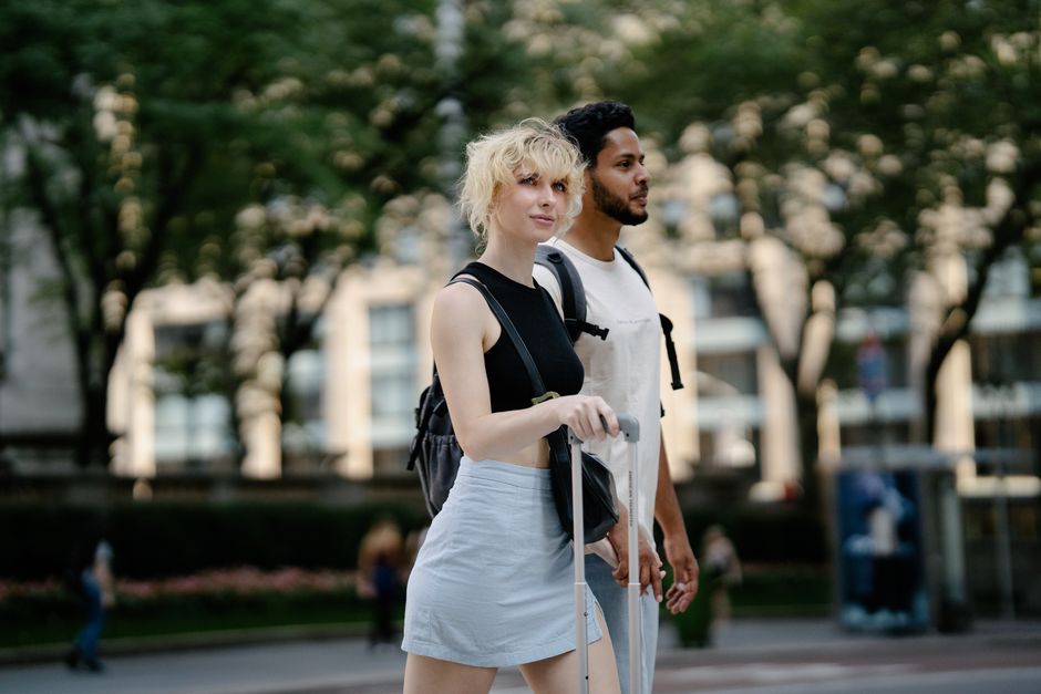 Una joven pareja disfruta de un día soleado caminando en un parque urbano con árboles verdes exuberantes.