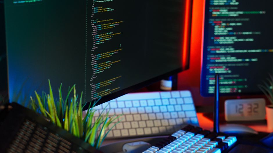 Un espacio de trabajo vibrante que muestra monitores de computadora con código, teclado y accesorios tecnológicos.